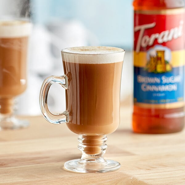 A glass cup of brown liquid next to a bottle of Torani Brown Sugar Cinnamon Flavoring Syrup.