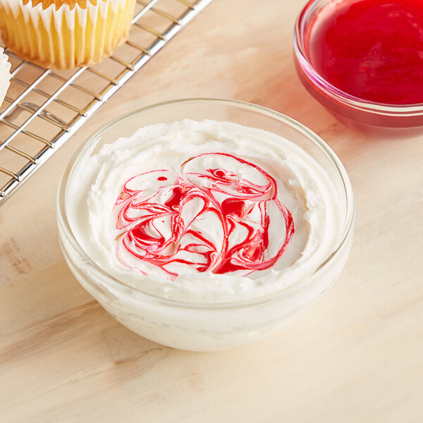 A bowl of white frosting with red swirls on top of it.