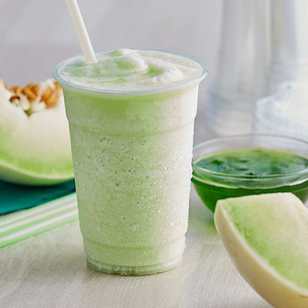 A green smoothie in a plastic cup with a slice of honeydew on the rim.