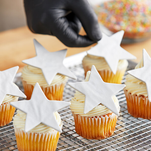 A hand in a black glove holding a star shaped cupcake with silver frosting.