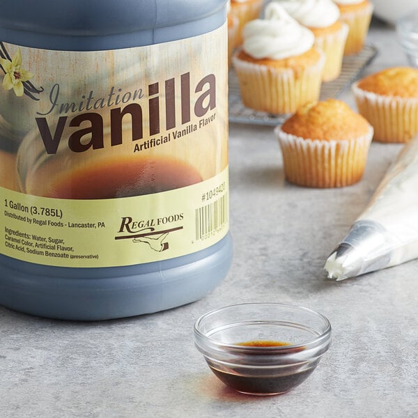 A bottle of Regal Imitation Vanilla next to cupcakes with frosting on a table.