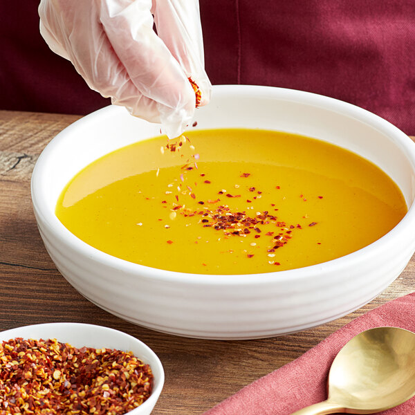 A person pouring Regal Mild Crushed Red Pepper into a bowl of soup.