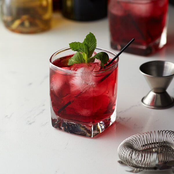 A glass of red liquid with ice and a straw with mint leaves.