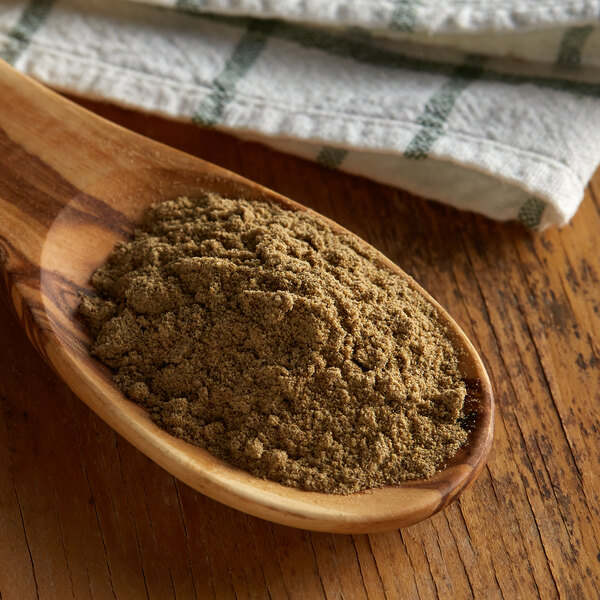 A spoon filled with Regal ground cardamom powder on a wood surface.