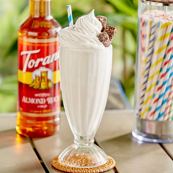 A glass of milk with Torani Almond Roca flavoring syrup and a straw on a coaster.