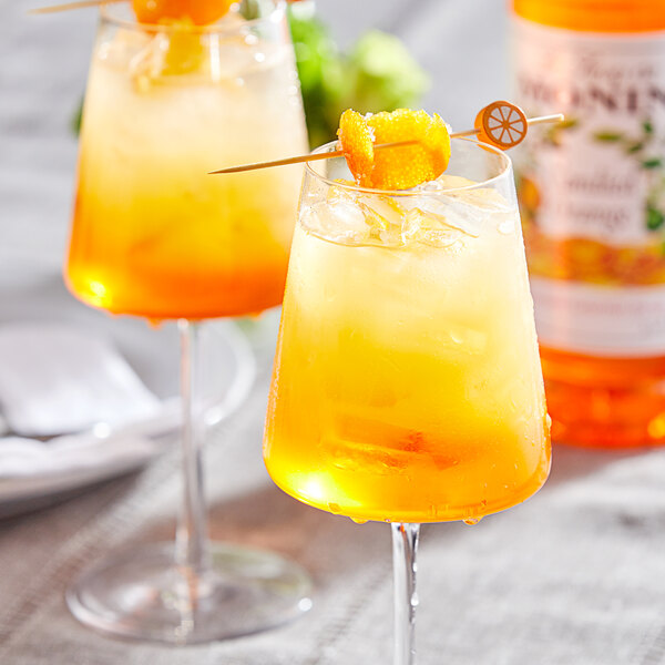 Two glasses of Monin candied orange drinks with fruit on a toothpick.