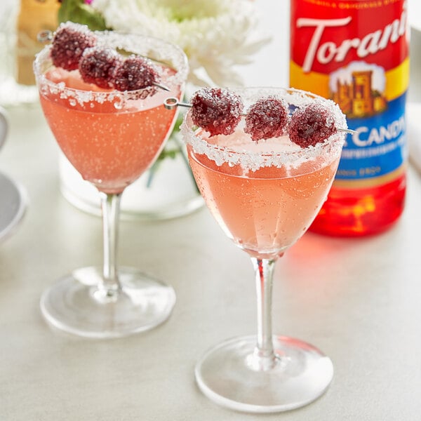 Two glasses of pink liquid with raspberries on top.