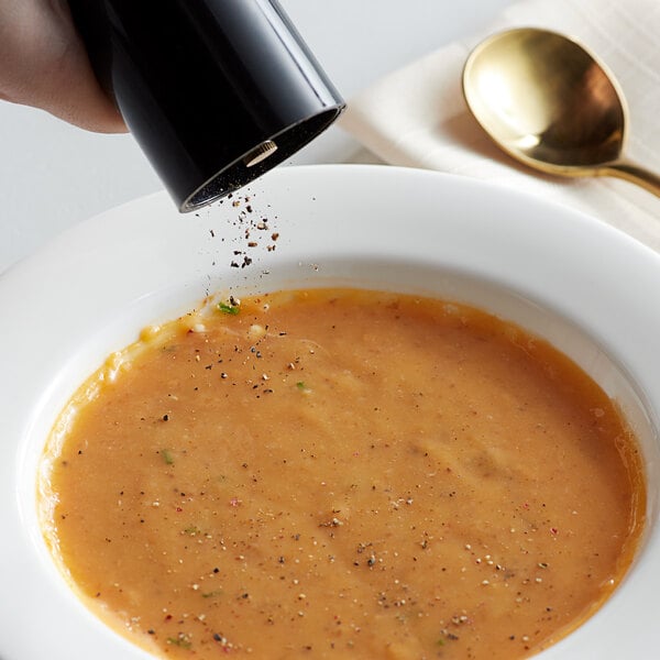 A hand using a pepper mill to sprinkle Regal Gourmet Peppercorn Medley into a bowl of soup.
