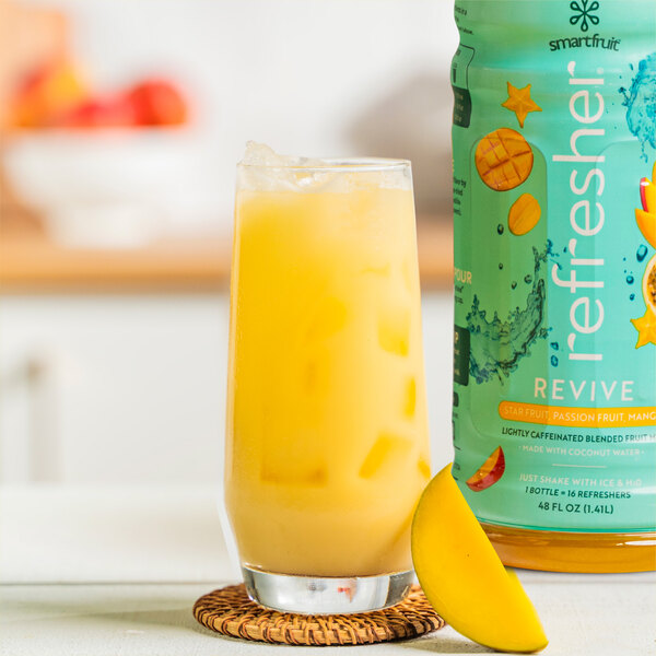 A close up of a yellow glass of Smartfruit Mango Passion Fruit Reviver next to a fruit slice.