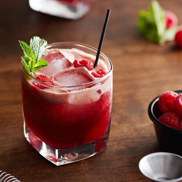 A glass of Monin raspberry fruit puree cocktail with ice and raspberries.