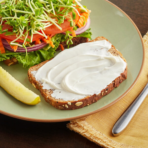 A plate with a sandwich and a pickle on it with white cream on the sandwich.