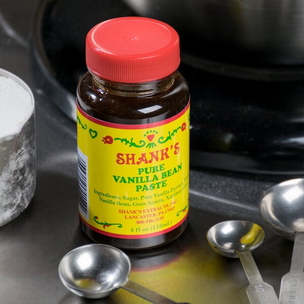 A jar of Shank's vanilla bean paste on a table with measuring spoons.