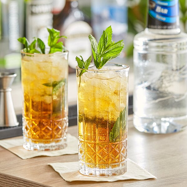 Two glasses of drinks with mint leaves on top on a table in a cocktail bar.