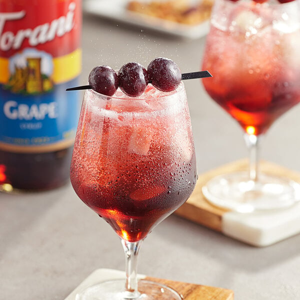 A glass of red liquid with grapes on the rim.