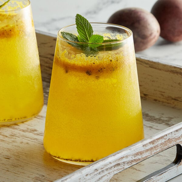 Two glasses of yellow liquid with mint leaves on top sitting on a table in a juice bar.