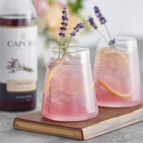 Two glasses of pink drinks with lavender and lemon slices on a wooden board.