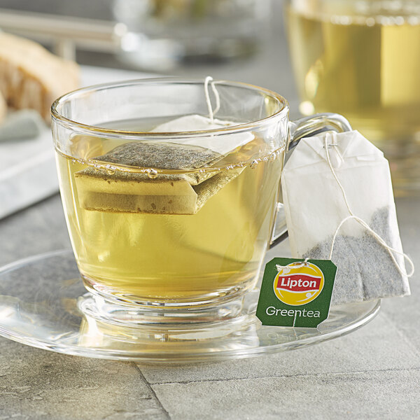 A glass cup of Lipton Classic Green Tea with a tea bag in it.