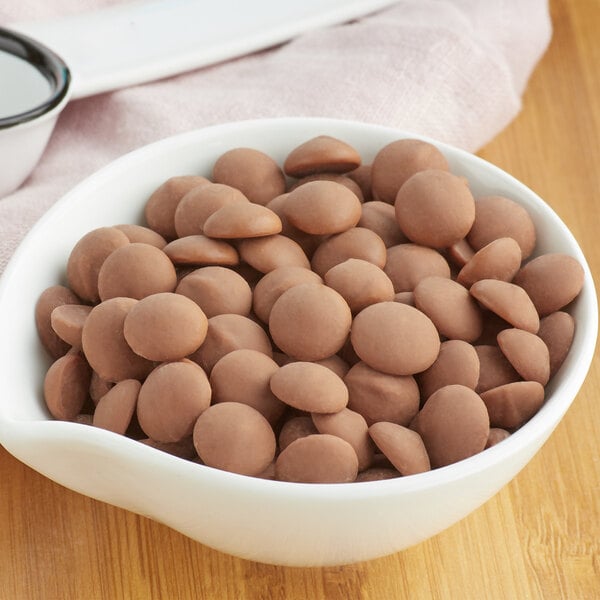 A white bowl of Callebaut milk chocolate chips on a wooden table.