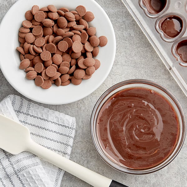 A bowl of Callebaut milk chocolate chips next to a bowl of brown liquid and a spoon.