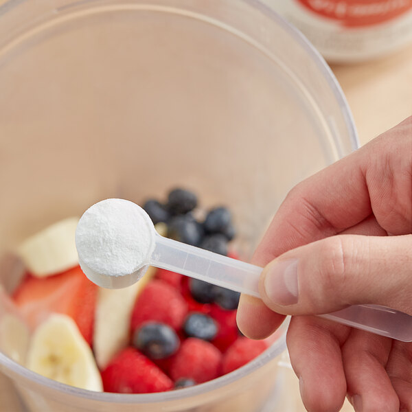 A hand holding a spoon of Add A Scoop Vitamin C Blend supplement powder.