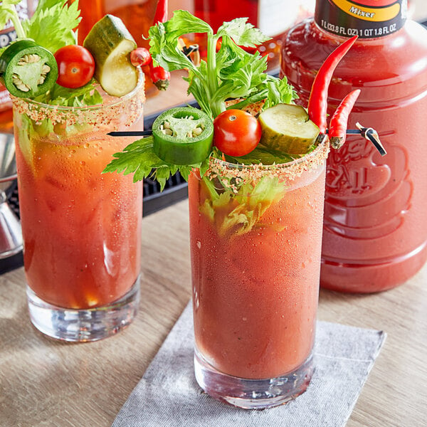 Two glasses of bloody mary with vegetables on top.