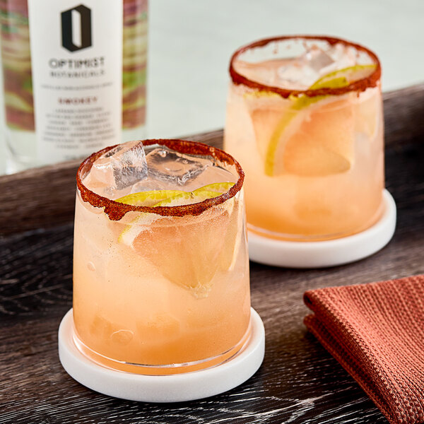 A table with two glasses of Optimist Botanicals Smokey non-alcoholic spirit with ice and lemon.