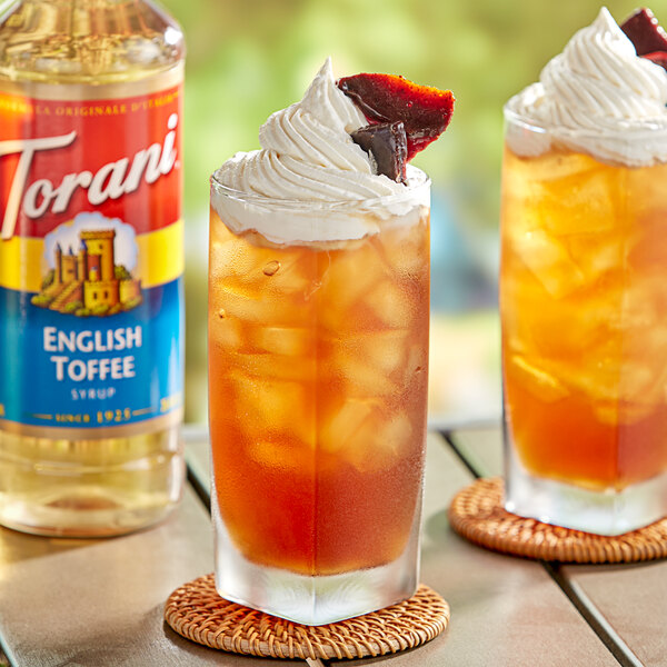 A glass of iced tea with whipped cream and a cherry and a bottle of Torani English Toffee Flavoring Syrup.