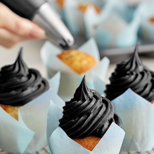 A hand using a Chefmaster Black Diamond Liqua-Gel to frost a cupcake with black frosting.