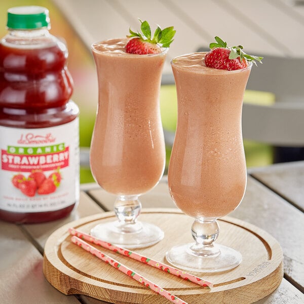Two glasses of strawberry smoothie with straws on a wooden surface.