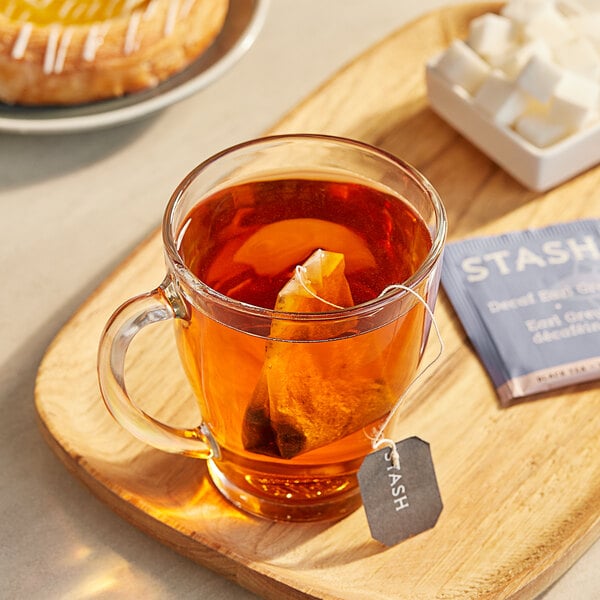 A wooden tray with a glass mug of Stash Decaf Earl Grey tea and a Stash Decaf Earl Grey tea bag next to a pastry.