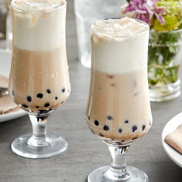 Two glasses of brown sugar milk tea with black bubbles on a table.