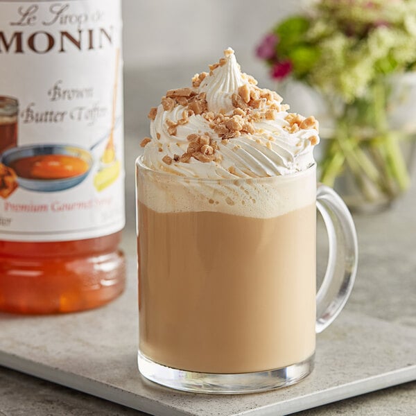 A glass mug of Monin brown butter toffee drink with whipped cream and nuts.