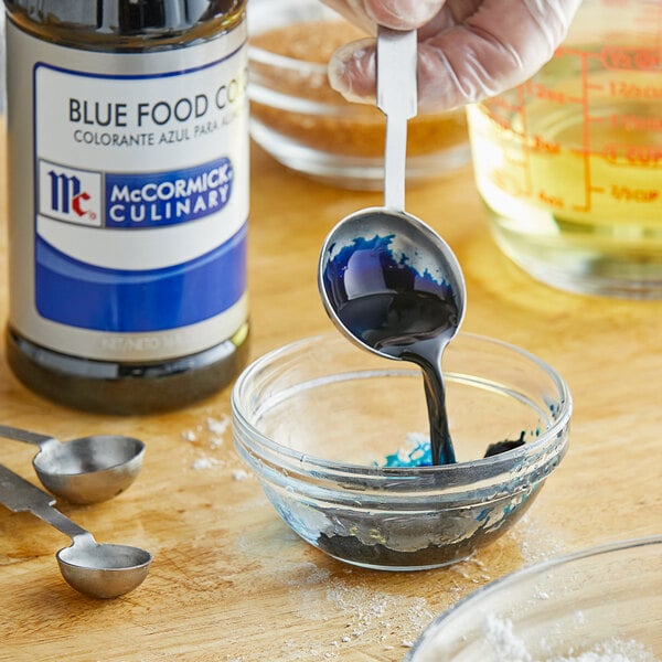 A person pouring McCormick blue food coloring into a bowl.