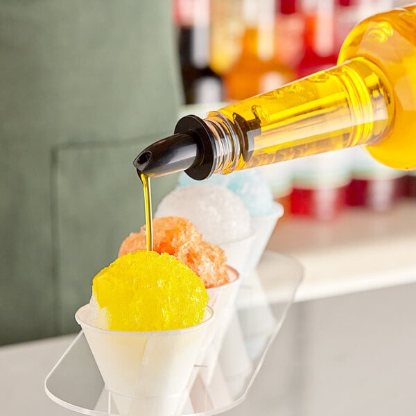 A bottle of Hawaiian Shaved Ice Banana syrup being poured over a snow cone.