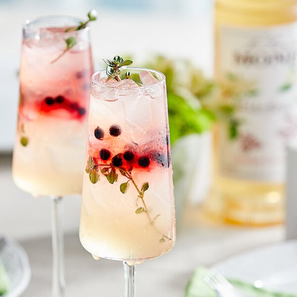 Two glasses of a drink with elderflower syrup, berries, and mint.