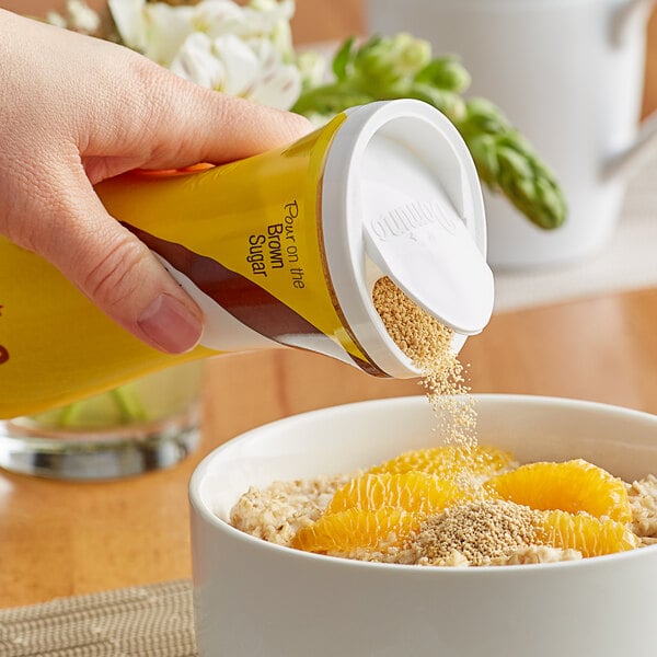 A hand pouring Domino brown sugar into a bowl of oatmeal with oranges.