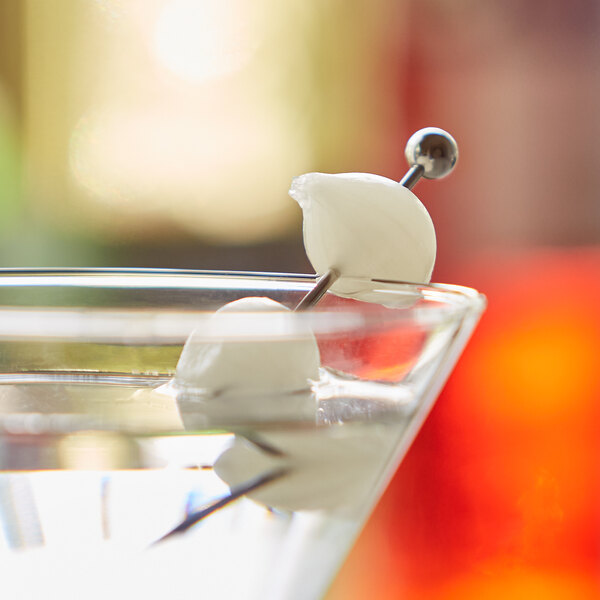 A martini glass with a Regal Cocktail Onion in it on a table in a cocktail bar.