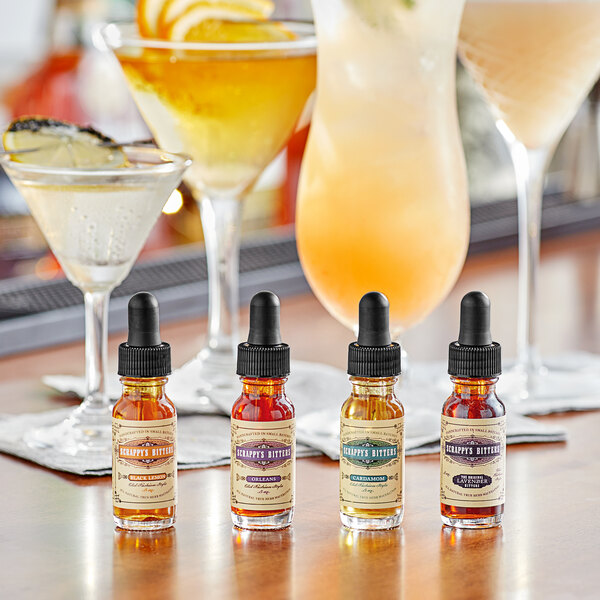 A table with bottles of Scrappy's Bitters next to glasses of different cocktails.