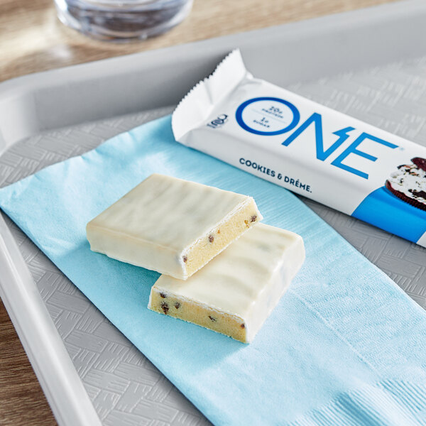 A white ONE Cookies and Creme protein bar on a blue napkin next to a cup of coffee.