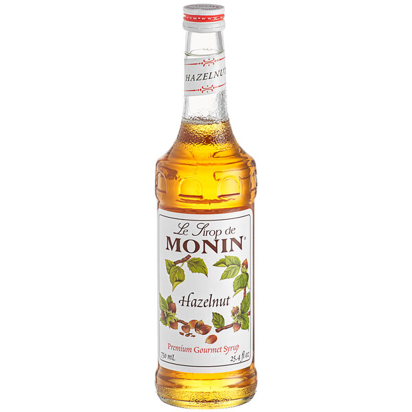 A Monin bottle of brown liquid with a white label.