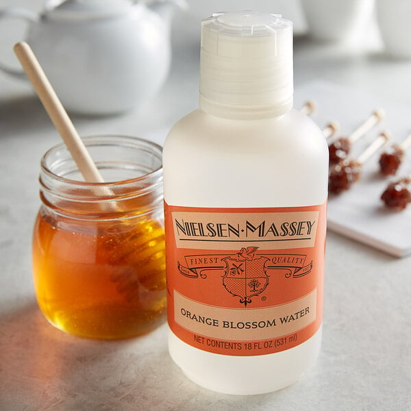 A bottle of Nielsen-Massey Orange Blossom Water next to a jar of honey.