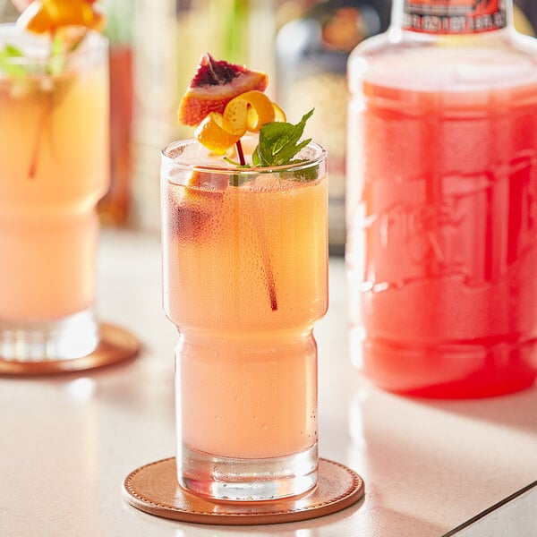 A glass of red liquid with fruit and mint on top.