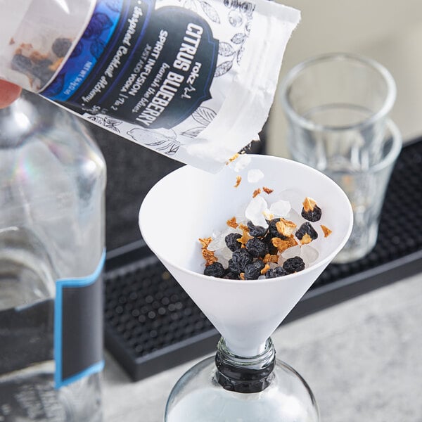 A hand pouring a mixture of blueberries into a glass funnel.