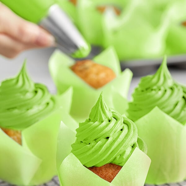 A hand using Chefmaster Neon Brite Green food coloring to decorate cupcakes with green frosting.