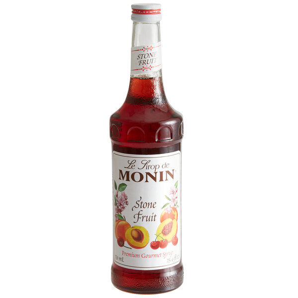 A Monin bottle of red sweet peach syrup with a white label.