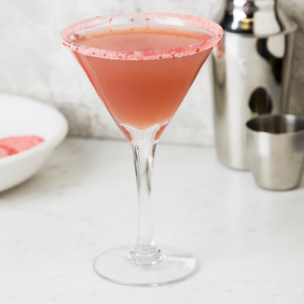 A hand rimming a cocktail glass with pink and white Rokz Cranberry Cosmo rimming sugar.