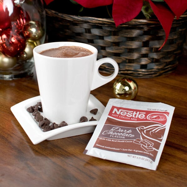 A white mug of Nestle hot chocolate on a plate with a packet of dark chocolate chips.