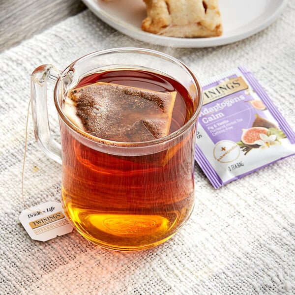 A glass mug of brown Twinings Fig & Vanilla tea with a tea bag on a white cloth.