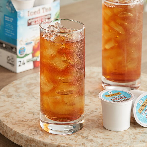 A glass of Twinings iced tea with ice next to a box of Twinings tea pods.