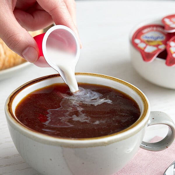 A person pouring International Delight sweet and creamy non-dairy creamer into a cup of coffee.